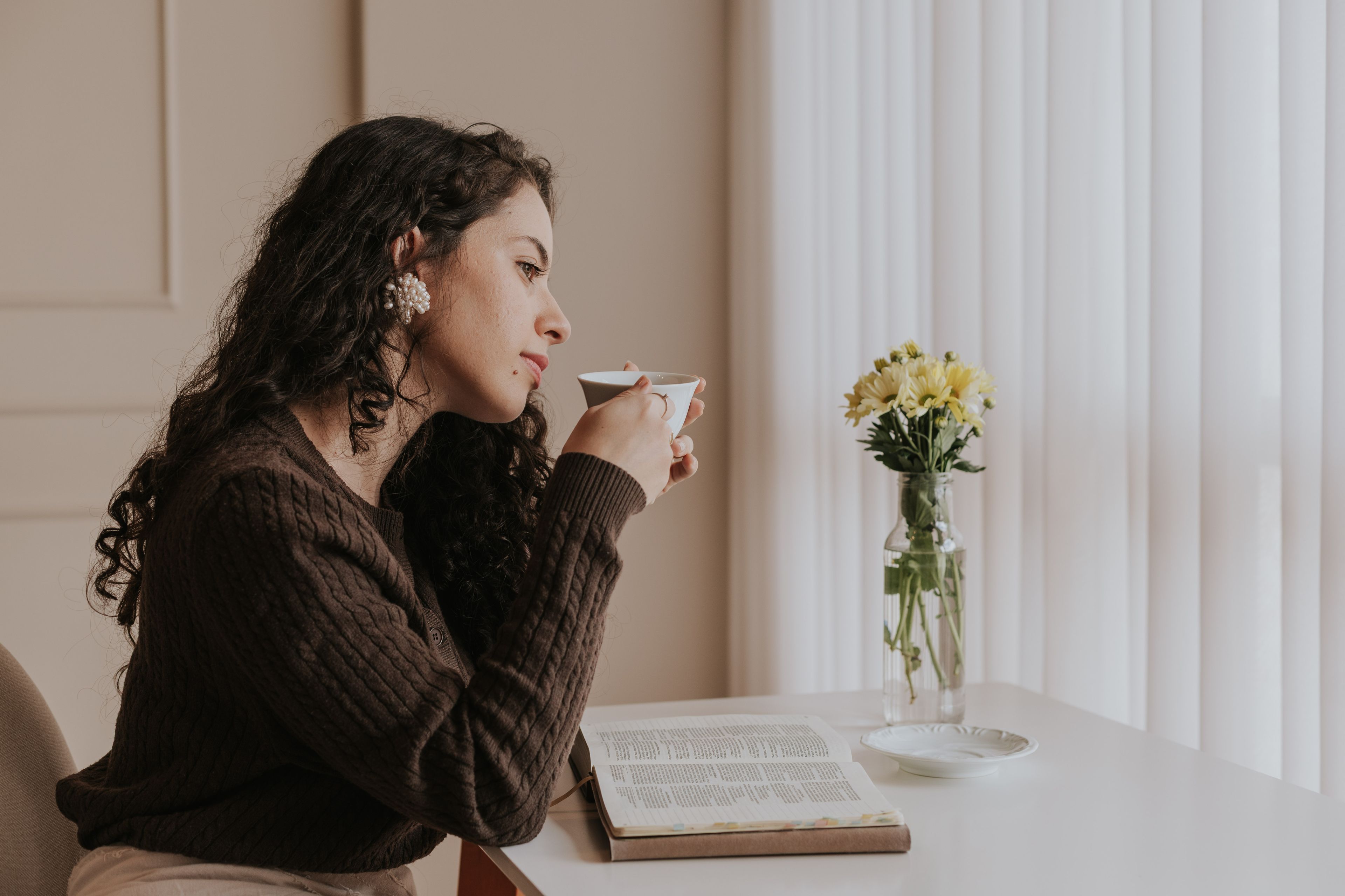 A person pausing with a cup of tea and an open book in soft window light