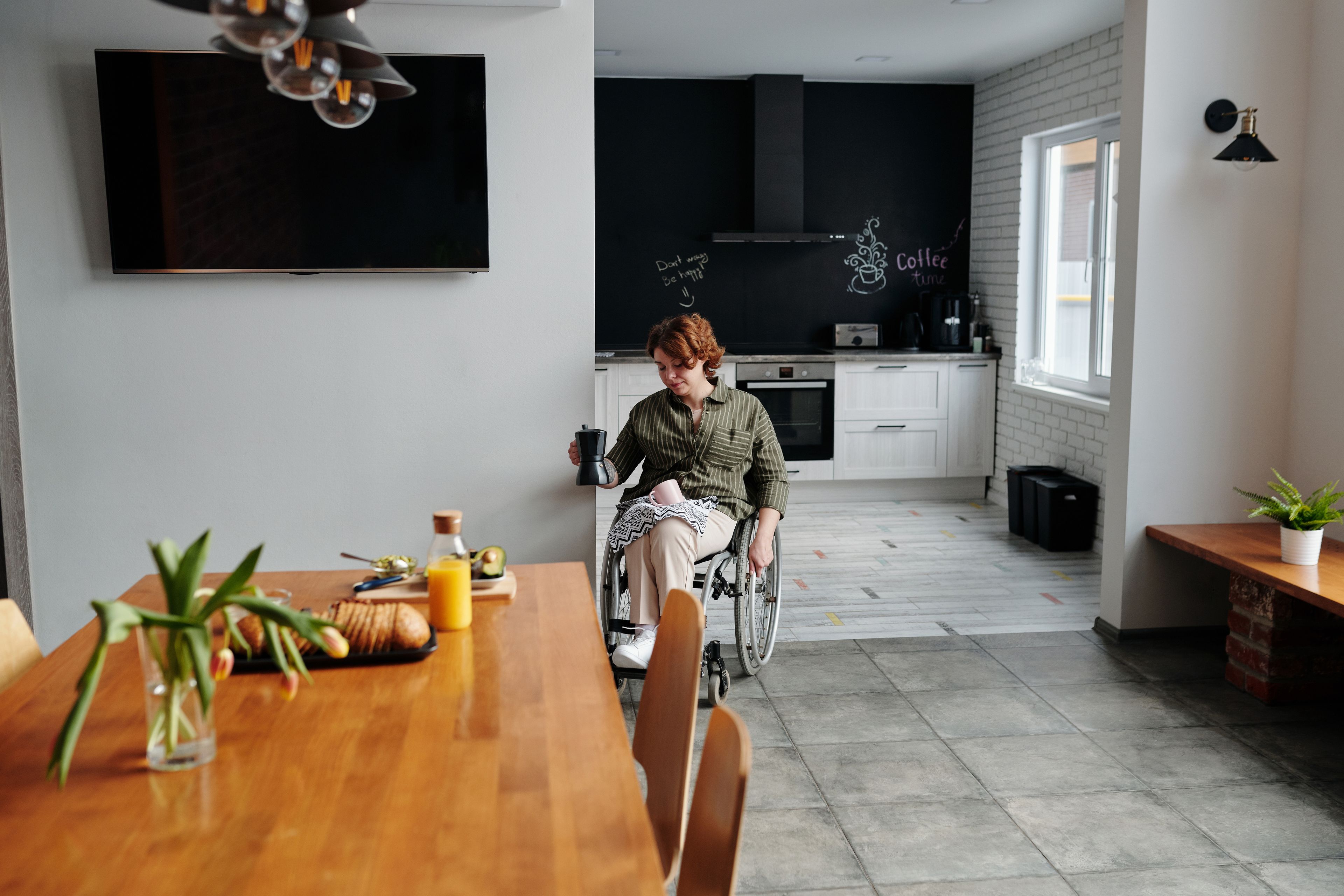 A woman using a wheelchair makes coffee in her kitchen at home