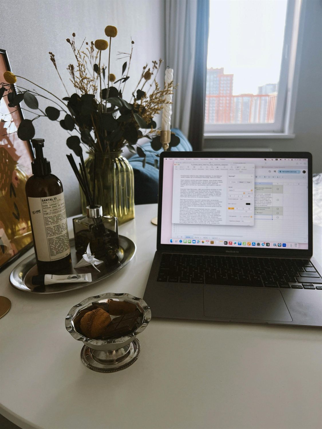 A calm home workspace with a laptop, books and a plant beside a window in warm light