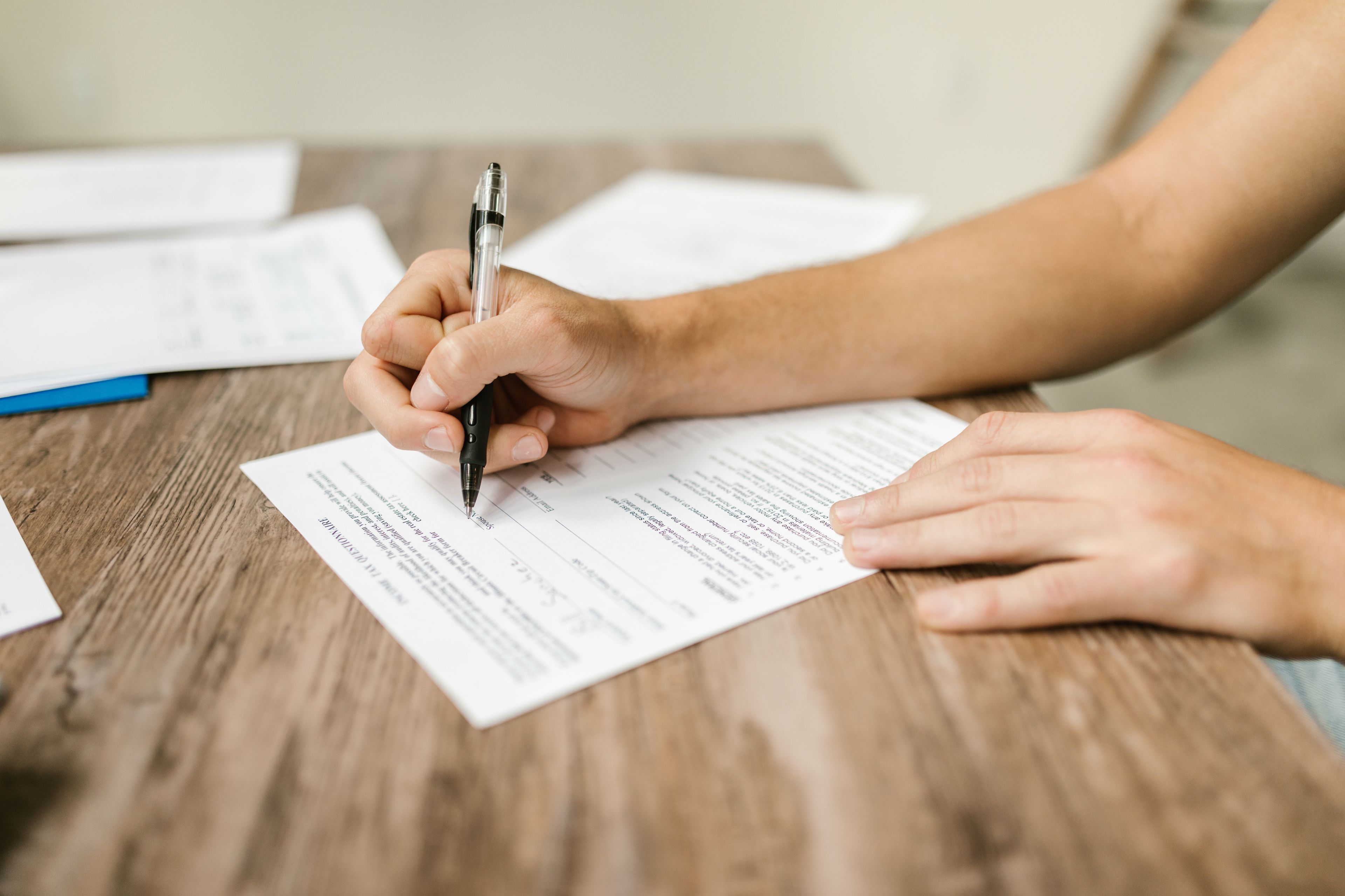 Hands completing a paper form with a pen at a wooden desk