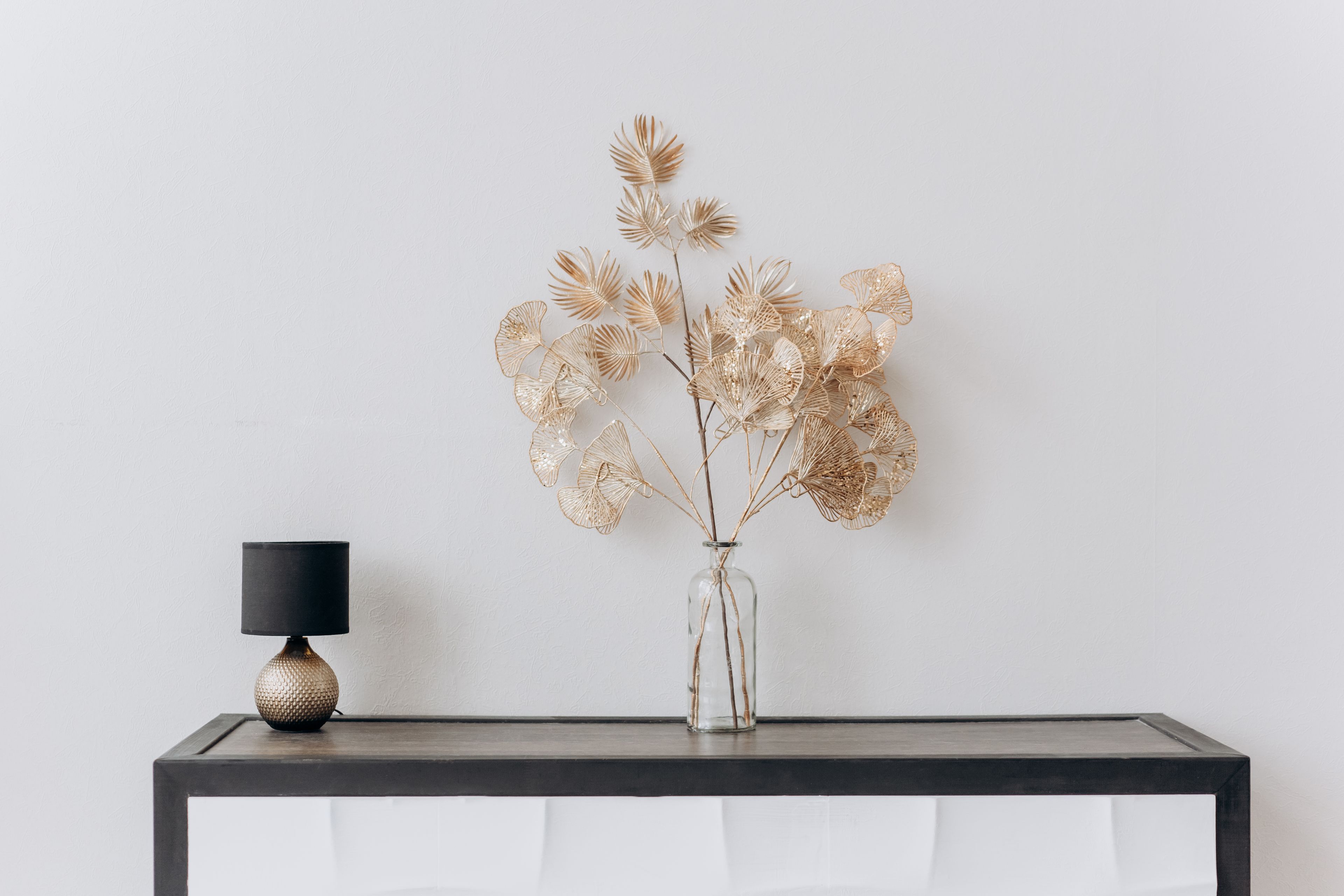 Dried golden stems in a clear glass vase beside a small lamp on a console