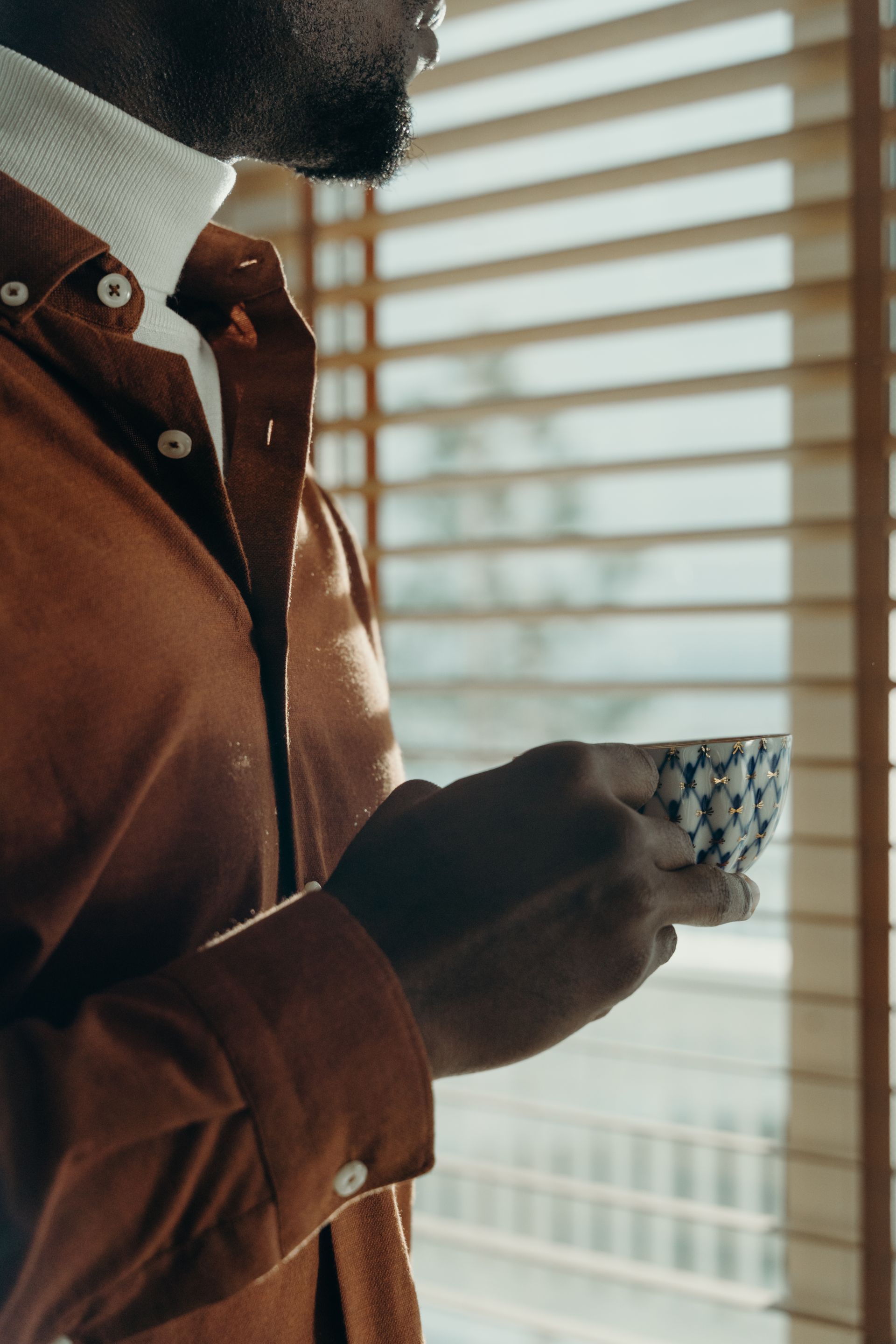 A person holding a cup of tea by a sunlit window in a quiet, reflective moment